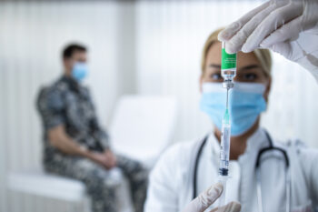 Vaccination of the military against corona virus. Doctor holding bottle and syringe and preparing vaccine shot for the soldier in uniform during corona virus epidemic.